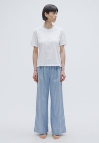 T-shirt blanc en coton associé à un pantalon large à rayures bleues. Le t-shirt a des manches courtes et une coupe décontractée ; le pantalon a une texture lisse.