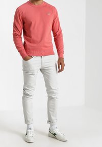 Sudadera de cuello redondo de color coral con puños acanalados, combinada con jeans blancos y zapatillas blancas con detalles en verde. Diseño sencillo y casual.