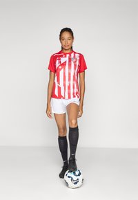 Rød- og hvitstripete fotballdrakt med grafisk mønster, kombinert med hvite shorts og svarte sokker, stående på en fotball.