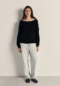 Svart oversize-tröja, ljusblå jeans med rak ben och svarta flätade sandaler. Tröjan har en vid halsringning och långa ärmar.