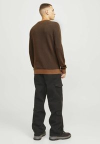Pulover tricotat maro cu un model texturat, asortat cu pantaloni cargo negri cu buzunare și o croială relaxată. Încălțăminte neagră cu vârful deschis.