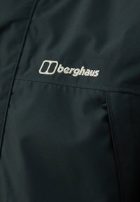 Crna vodootporna jakna glatke teksture, s vezanim logotipom svijetle boje i naglascima na patentnim džepovima.