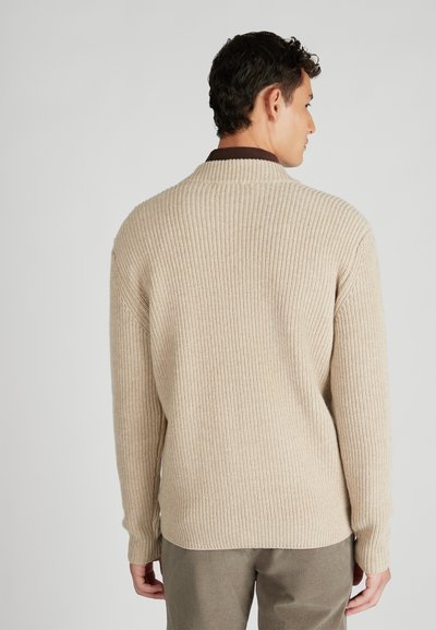 Beige geribde trui met hoge kraag, met lange mouwen en een losse pasvorm, textuur stof en een bruine accent bij de kraag.