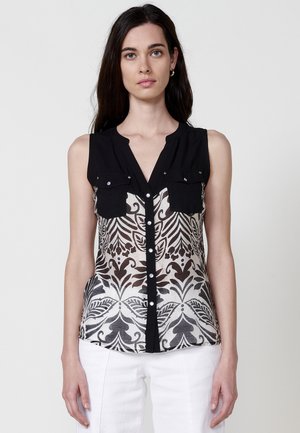 Schwarzes ärmelloses Blusenshirt mit Knopfleiste und zwei Brusttaschen. Der untere Teil hat ein kontrastierendes florales Muster in Weiß und Schwarz.