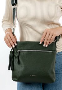 Green textured leather crossbody bag with a zippered pocket and tassel detail, featuring a long adjustable strap and logo accent.