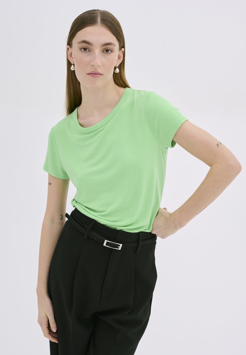Tricou verde deschis din material neted, cu decolteu rotund și mâneci scurte, asortat cu pantaloni negri cu talie înaltă și o curea.