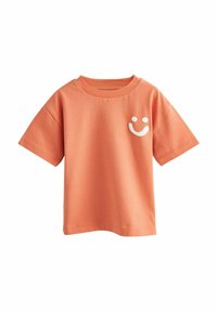 Oranssi puuvillainen t-paita lyhyillä hihoilla, jossa on vasemmassa rinnassa valkoinen hymyilevä naama painettuna ja pyöreä kaula-aukko.