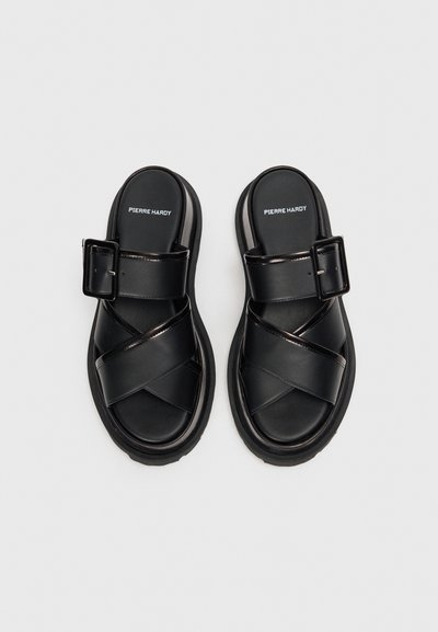 Svarta sandaler med korsade remmar, justerbar spänne och tjock sula. Tillverkade av slätt läder med en matt finish. Varumärkeslogotypen synlig.