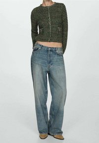 Cardigan court vert tricoté avec fermeture à boutons et deux poches avant, associé à un jean taille haute large bleu clair et des chaussures beiges.