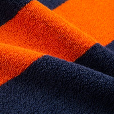 Πετσέτα με έντονες πορτοκαλί και ναυτικό μπλε ρίγες, με υφή βαριά και απαλής επιφάνειας, που παρουσιάζει ένα μαλακό, απορροφητικό μείγμα υφασμάτων.