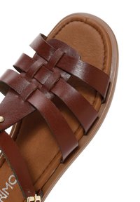 Sandale en cuir marron avec des brides tissées et une semelle rembourrée montrée en angle sur fond blanc.