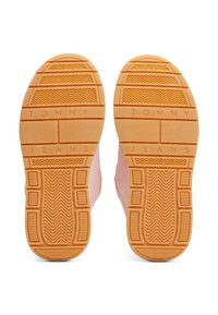 Semelles de chaussures avec une bande de caoutchouc orange comportant le texte « TOMMY JEANS » et des zones de grip à motif sur une base de chaussure rose clair.