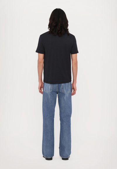Svart bomulls T-skjorte med korte ermer, kombinert med lyseblå vidbukse i denim. Synlig søm og fem lommer på buksen.