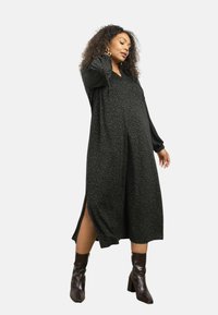 Černé midi šaty s zeleným leopardím potiskem, dlouhými rukávy, bočními rozparkami a volným střihem. Oblékněte k nim hnědé boty na podpatku.