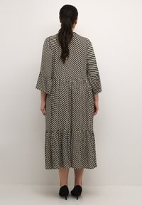 Schwarzes und weißes gemustertes Maxikleid mit dreiviertellangen, ausgestellten Ärmeln und volantsaum. Glattes Material, knielang und tailliert.