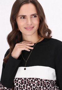 Schwarzes Langarmoberteil mit einem weißen horizontalen Streifen und einem unteren Abschnitt mit einem pinken Tierdruckmuster; Model trägt eine schlichte Halskette.