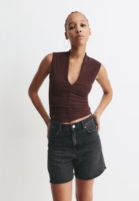 Braunes, strukturiertes ärmelloses Oberteil mit tiefem V-Ausschnitt, kombiniert mit hoch taillierten schwarzen Jeansshorts mit ausgefransten Säumen.