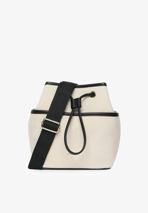 Eimer-Tasche aus Canvas in Creme mit schwarzem Rand, verfügt über einen Kordelzugverschluss und einen verstellbaren Träger mit einem Akzent aus goldfarbigem Metall.