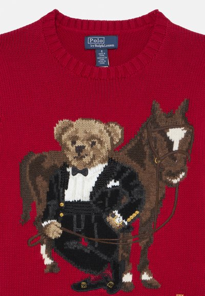 Červený pletený sveter s vyšívaným medveďom v smokingu vedľa hnedého koňa, doplnený o motýlika, hodinky a textúrované detaily.