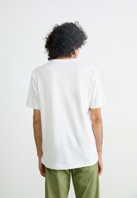 White cotton t-shirt with short sleeves and a crew neck, shown from the back. Simplistic design with a smooth texture.