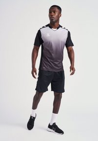 Sort og grå sportsjersey med gradientdesign, korte ærmer og v-hals. Akkompagneret af sorte shorts og sorte sneakers.