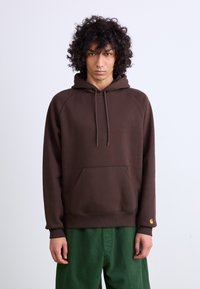 Brown hoodie with a front pocket, drawstring hood, and ribbed cuffs. Made of soft fabric; features a small gold logo on the left sleeve.
