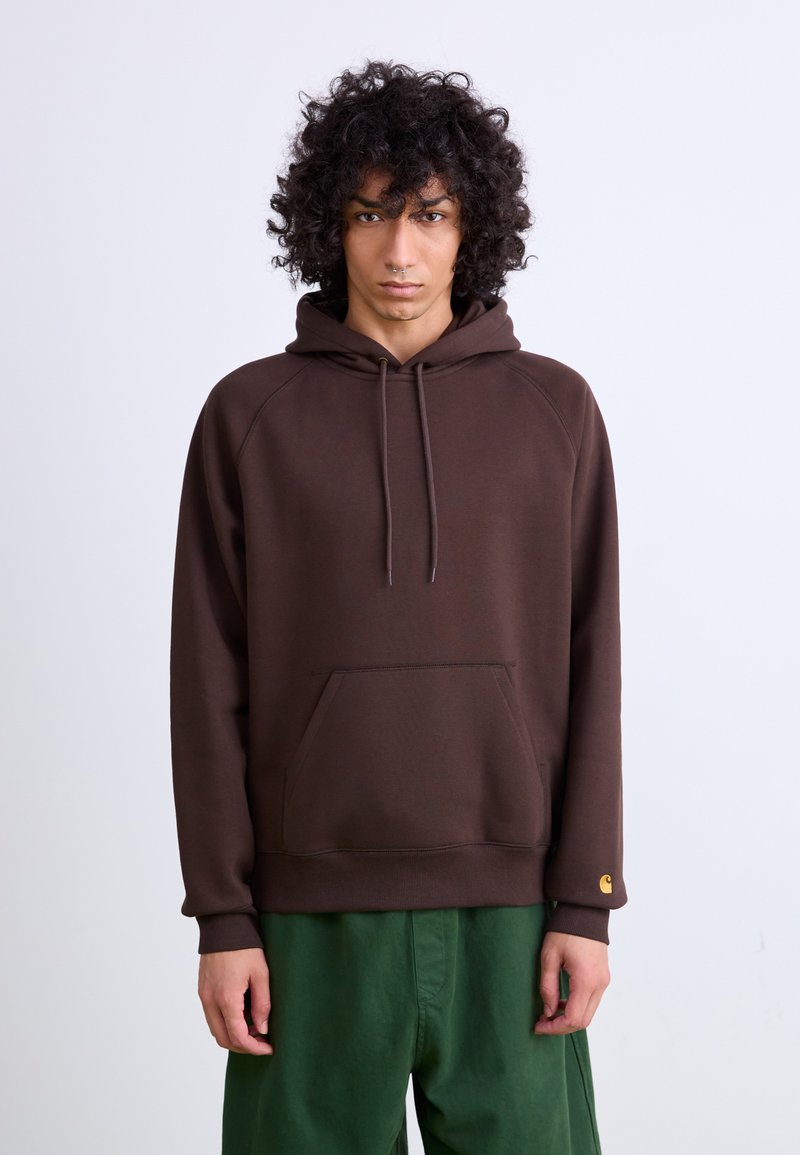 Brown hoodie with a front pocket, drawstring hood, and ribbed cuffs. Made of soft fabric; features a small gold logo on the left sleeve.