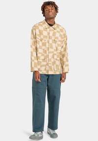 Beige ruuduline jakk kahe esiosa taskuga, koos tume türkiissiniste laia säärega pükstega ja hallide tossudega. Sile kanga tekstuur.