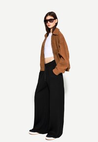 Brun mockaskinnjacka, vit kort topp och svarta vida byxor. Accessoarer inkluderar överdimensionerade solglasögon och vita sneakers med bruna accenter.