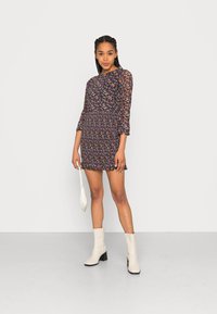 Vestido mini floral com fundo escuro, mangas longas transparentes, textura canelada e bainha com babados. Combinado com botas de tornozelo cream e uma clutch.