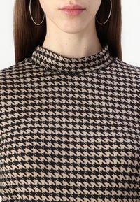 Geprinte coltrui met een houndstooth-patroon in zwart en beige. De stof lijkt zacht met een gladde textuur.