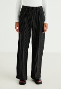 Black, wide-leg pants featuring vertical white pinstripes. Made of a lightweight material with an elastic waistband for comfort.