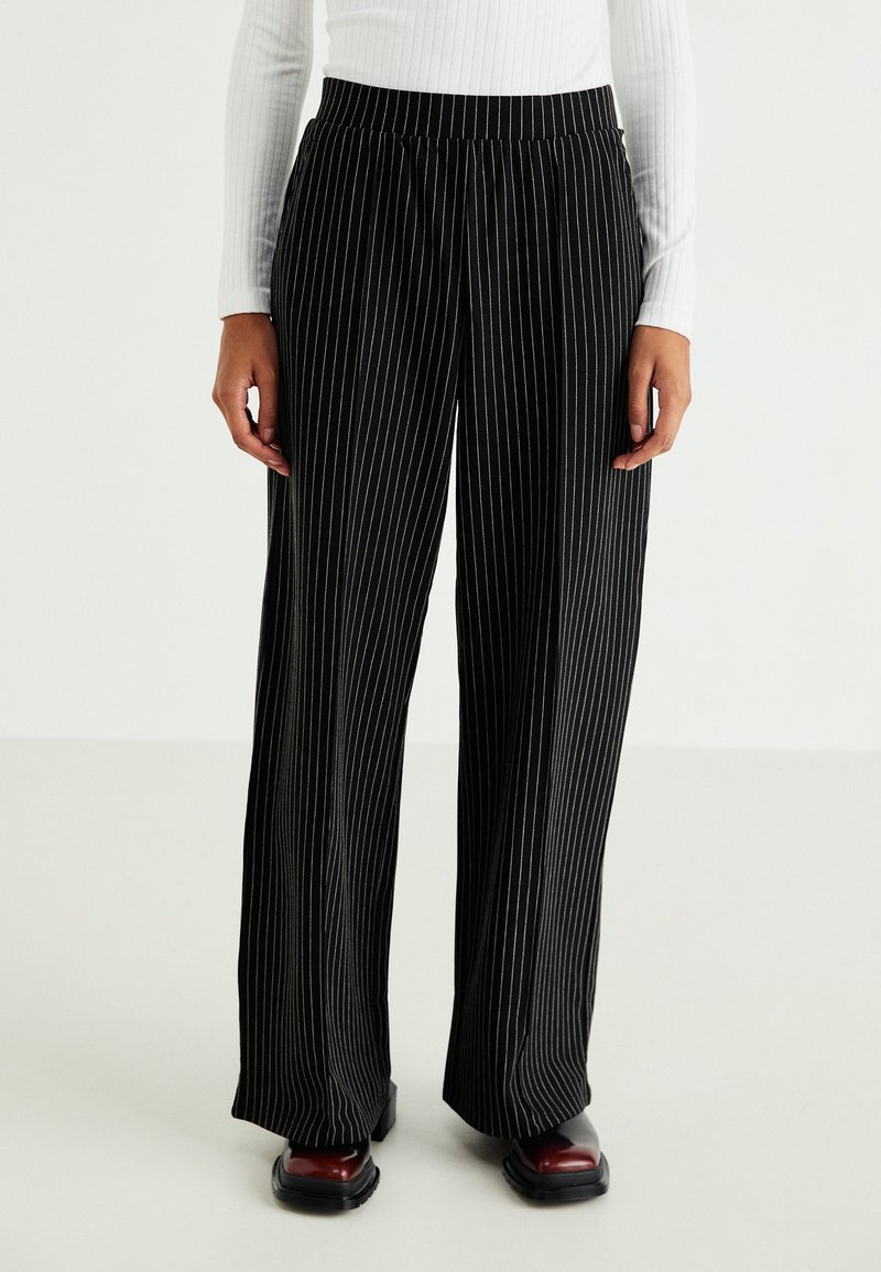 Black, wide-leg pants featuring vertical white pinstripes. Made of a lightweight material with an elastic waistband for comfort.