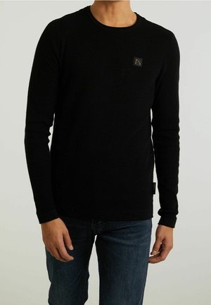 Maglione nero a maniche lunghe realizzato in un tessuto a maglia testurizzato. Presenta una piccola patch con il marchio sul petto e polsini e orlo a coste.
