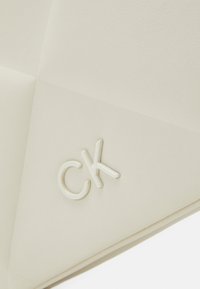 Biela koženka taška s prešívaným dizajnom, s vyvýšeným bielym logom "CK" na povrchu.