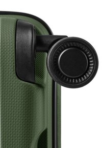 Gros plan d’un coin texturé d’une valise verte avec une roulette pivotante noire attachée pour rouler facilement.