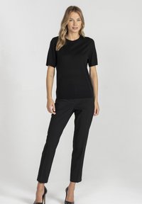 Czarny top z krótkim rękawem w połączeniu z dopasowanymi czarnymi spodniami i czarnymi butami na wysokim obcasie, prezentujący elegancki, monochromatyczny wygląd.