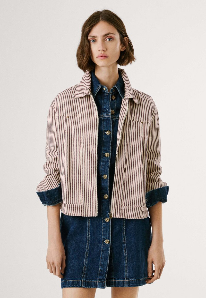 Giacca a cropped a righe in crema e rosso con maniche arrotolate, abbinata a un vestito in denim scuro con bottoni caratterizzato da una linea dritta e tasche frontali.