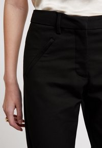 Černé kalhoty na míru vyrobené z hladké tkaniny, se slim fit střihem a nenápadnými bočními kapsami s plochým pasem.