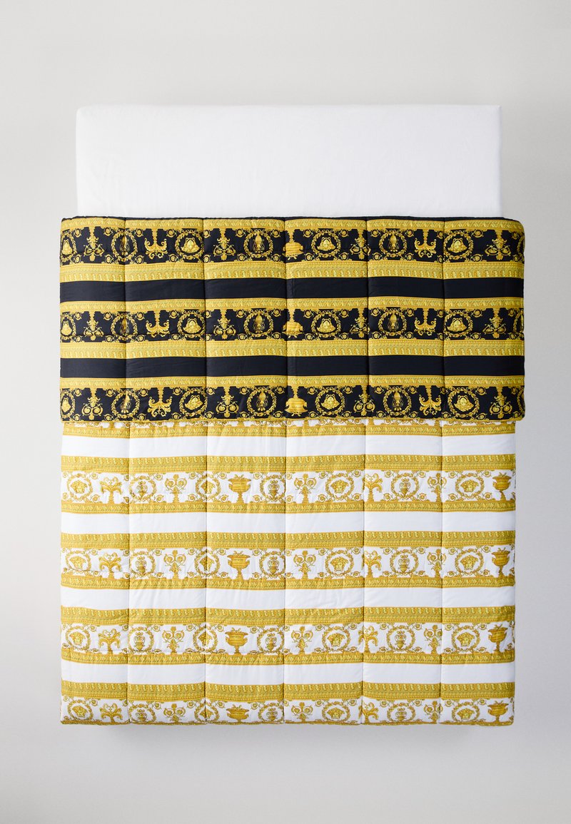 Prošívané povlečení s horní částí s černým a zlatým vzorem a dolní částí s bílým a zlatým vzorem, která obsahuje složité motivy.