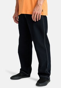 Črne denim hlače z belim šivom, ravne noge in trpežno blago. V kombinaciji s črnimi natikači in oranžno majico.