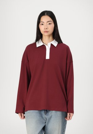 Bordeaux langermet polo skjorte med hvit krage, mykt stoff, avslappet passform og synlig knappestolpe. Brukt sammen med lyseblå jeans.