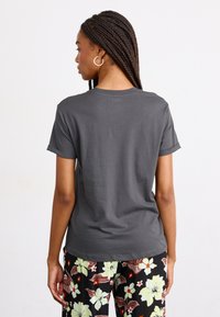 T-shirt gris à manches courtes avec un col rond et des manches retroussées, associé à un pantalon à motifs floraux présentant de grandes fleurs et des feuilles.