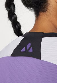 Lilla og svart treningsgenser med teksturert mesh-design, med fremtredende fargeblokker og en lilla logoakcent på baksiden.