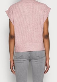 Ljusrosa ribbad stickad topp med hög halsringning, korta ärmar och tight midja. Kombinerad med grå jeans, visar bakvy.