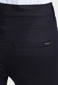 Dark denim jeans with a fitted design, featuring a back pocket and subtle stitching detail. The fabric appears smooth and durable.