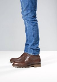 Braune Leder-Stiefeletten mit strukturierter Oberfläche, mit runder Spitze, Schnürverschluss und robuster Sohle, kombiniert mit blauen Jeans.