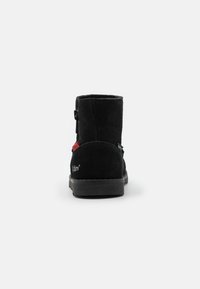 Bottes noires en suede avec une finition texturée, présentant une fermeture éclair latérale et un accent rouge contrastant. Semelle en caoutchouc épaisse pour la durabilité.