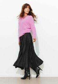 Pull rose en tissu duveteux associé à une jupe plissée noire ornée de points argentés, complété par des bottes noires à talons montant jusqu'aux genoux.