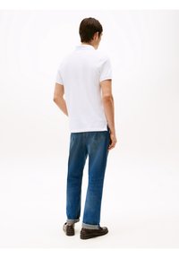 Bílá polokošile, modré džíny z denimu a tmavé boty. Polokošile má krátké rukávy a plochý límec; džíny jsou rovného střihu s vyhrnutými lemy.